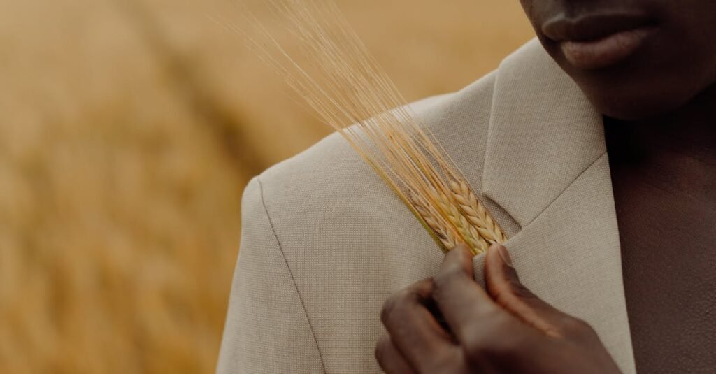 Close-up of a man in a suit holding wheat stalks in a field, showcasing autumn fashion.