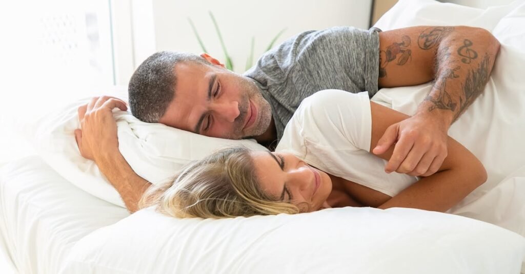 A loving couple rests together in bed with soft pillows, enjoying a peaceful moment.
